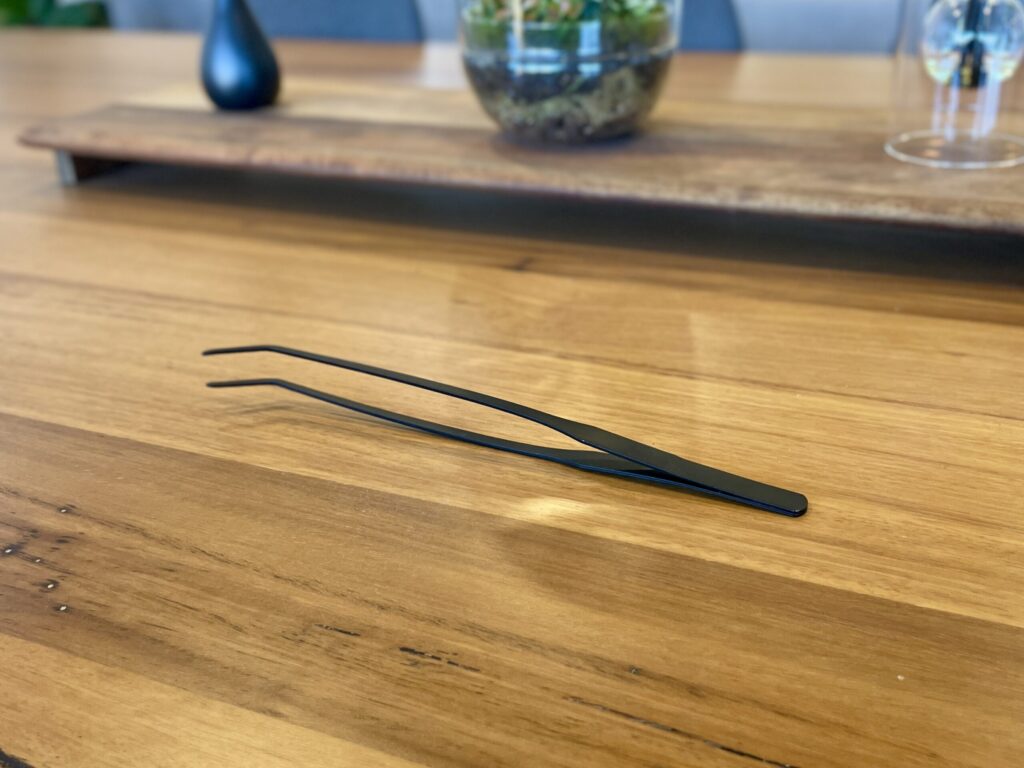 Eko Lab premium black stainless steel tweezers, on a wooden table